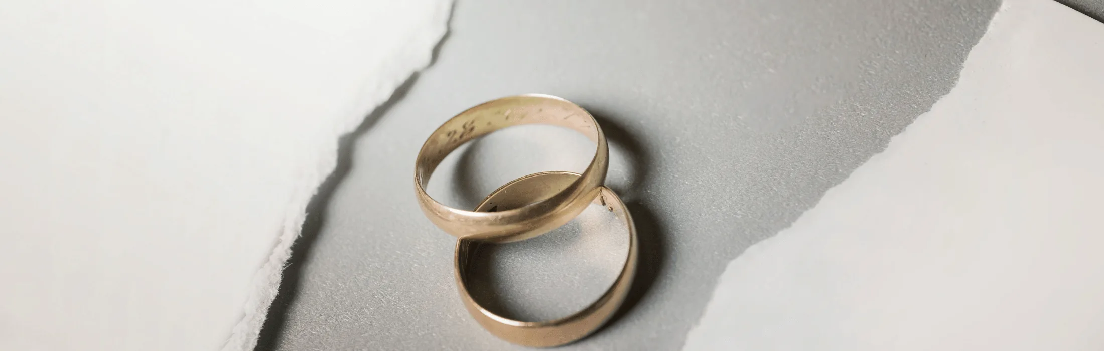 Two gold wedding bands intertwined on a light marble surface, symbolizing marriage or commitment.