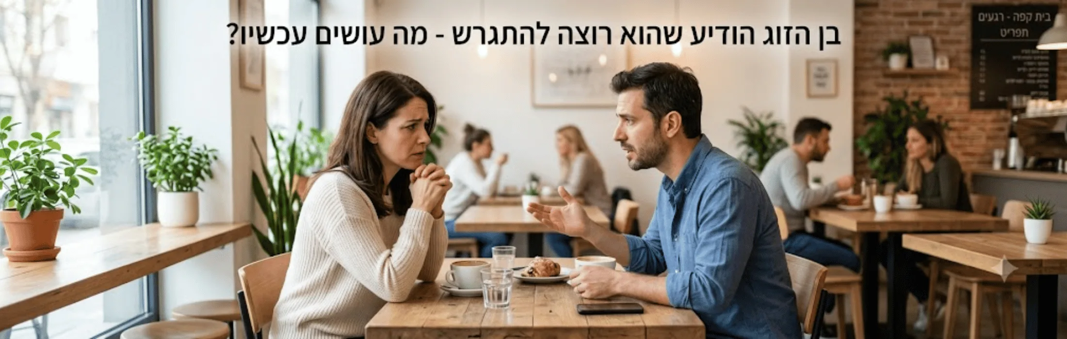 Two adults sit at a wooden table in a cafe, deeply engaged in conversation over coffee and a pastry as others chat in the background.