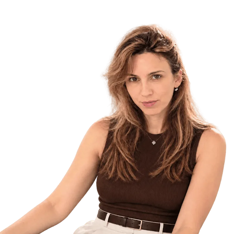 Portrait of a woman with long brown hair, wearing a sleeveless brown top and white belt, looking at the camera.